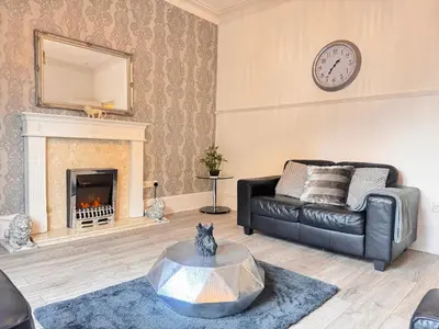 a living room with a black leather couch and a fireplace at THE LION’S REST - BOUTIQUE APARTMENT SUITE. in Port Glasgow
