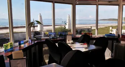 a restaurant with a table and chairs and a view of the beach at Argyll Hotel in Bellochantuy