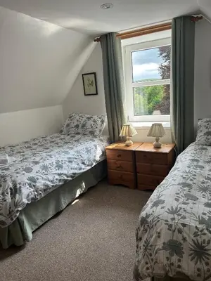 a bedroom with two beds and a window at Rowan Cottage in New Galloway