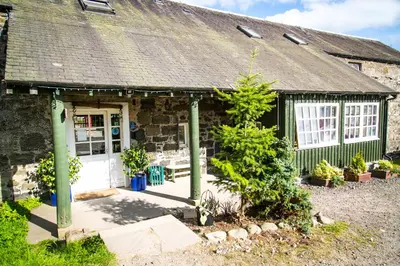 a stone cottage with a white door and some plants at Comrie Croft in Crieff