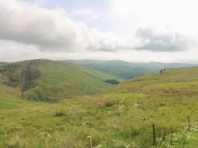 a green hillside with mountains in the background at Penthouse St Mary's Church in Moffat