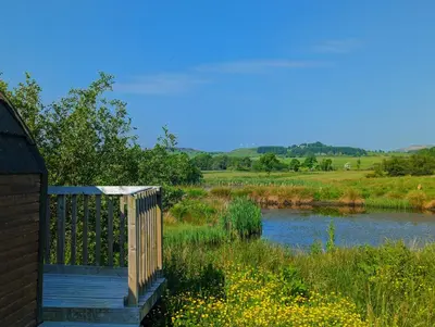 a wooden bridge over a river next to a field at Pond View Pod 1 with Outdoor Hot Tub - Fife - Loch Leven - Lomond Hills in Kelty