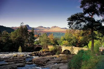 a bridge over a river with mountains in the background at Cosy & compact Rowan Lodge no2 in Killin