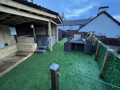 a backyard with green grass and a patio with a grill at Amazing Alps and Loch views - HOT TUB and pet friendly in Arrochar