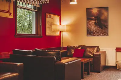 a living room with leather furniture and a red wall at Crianlarich Youth Hostel in Crianlarich