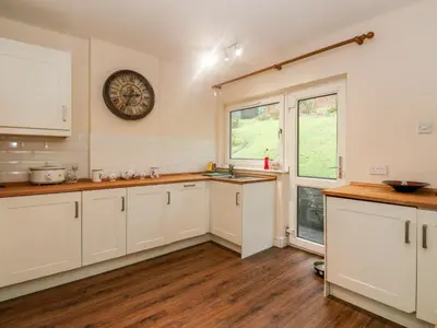 a kitchen with white cabinets and a clock on the wall at Glenfinglas Dam Cottage in Callander