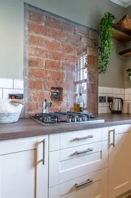 a kitchen with white cabinets and a brick wall at The Stirling Townhouse in Stirling