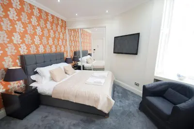 a bedroom with a bed and a chair and a television at Palmerston Suites in Edinburgh