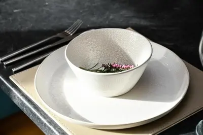 a white bowl on a plate with a fork at Rowan Tree Apartment - Modern Apartment, Free Parking & Views in Oban
