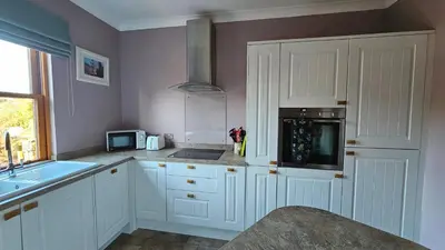 a kitchen with white cabinets and a sink and a microwave at Beautiful self contained apartment with garden in Glasgow