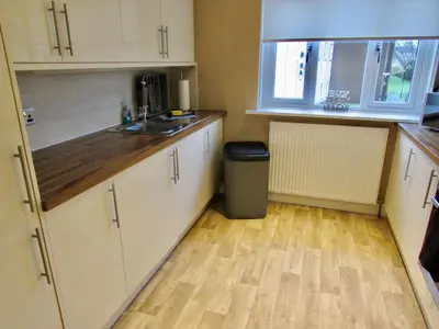 a kitchen with white cabinets and a wooden floor at Levenview Holiday Apartment Loch Lom in Balloch
