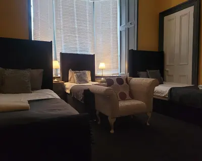 a room with three beds and a chair and a window at Stay - Gilmore Guesthouse in Edinburgh