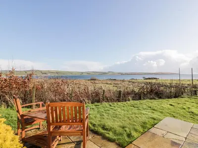 a wooden bench sitting in the grass near a lake at Ettrick Cottage in Port Bannatyne