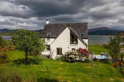 a white house on a grassy hill with a boat at Seabank Lochside Farmhouse in Oban