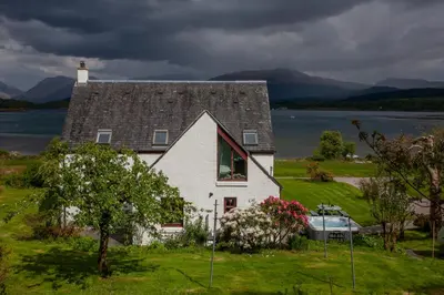 a white house on a hill with a boat in front of it at Seabank Lochside Farmhouse in Oban