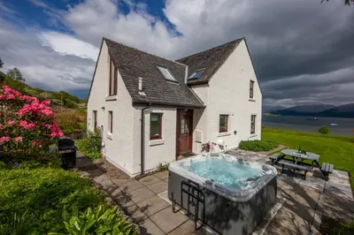 a house with a hot tub on a patio at Seabank Lochside Farmhouse in Oban