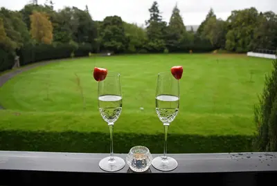 two wine glasses sitting on a table with a green field at Gleneagles Luxury Apartment in Auchterarder
