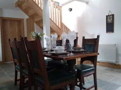 a dining room table with chairs and a wooden table and stairs at Auchnabreac Cottage in Carradale