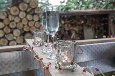a table with two wine glasses and a candle at 1-Bed Cabin 2 adults Wood Burning Hot Tub & Fire in Carluke