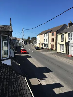 an empty street in a town with houses and a red car at RoSE COTTAGE THREE BEDROOM HOUSE WITH PARKING Christmas Special in Carsphairn