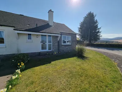 a house with a grassy yard next to a road at Lavender Cottage with Parking and Beautiful Views Christmas Special in Carsphairn