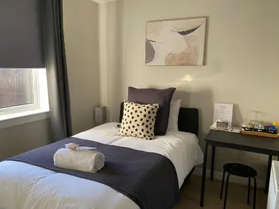 a bedroom with a bed with a blue blanket and a table at Peacock Guest House in Largs