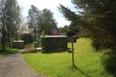 a sign in the grass in front of a tiny house at Woodland Hazel Lodge in Killin