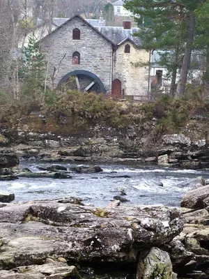 an old stone building sitting next to a river at Woodland Hazel Lodge in Killin