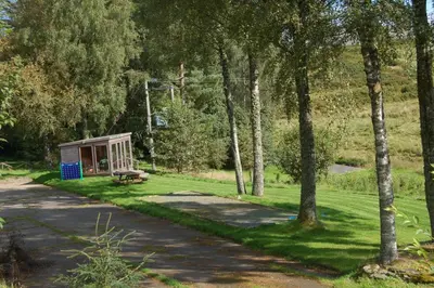 a park with a bench in the grass with trees at Woodland Spruce Lodge in Killin