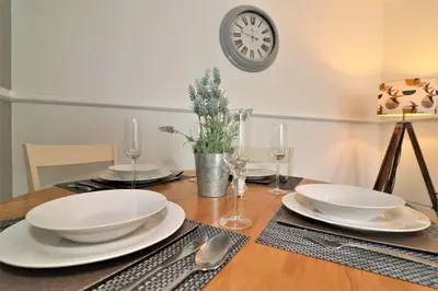 a dining room table with white dishes and a clock on the wall at Signature - Troon View in East Kilbride