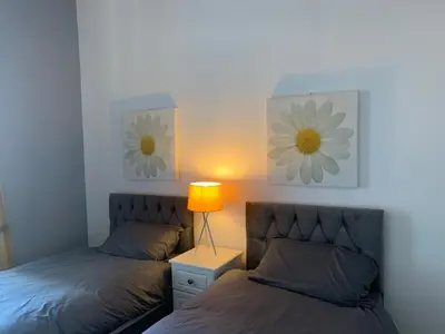 two beds in a bedroom with a lamp and flowers on the wall at Ayr Apartment with Sea and Countryside views in Ayr