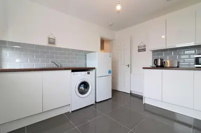 a kitchen with white cabinets and a washer and dryer at Signature - Newbattle House in Chapelhall