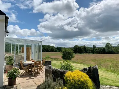a patio with a table and chairs and a field at Blair Cottage in Rowardennan
