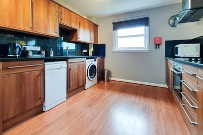 a kitchen with wooden cabinets and a washer and dryer at Hilton Wynd Apartment in Rosyth