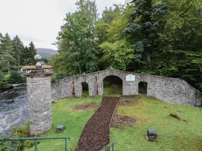an old stone building on a hill with a bridge at Millmore Cabin in Killin