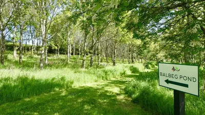 a sign for a black pond in a field with trees at Balcraig House in Maybole