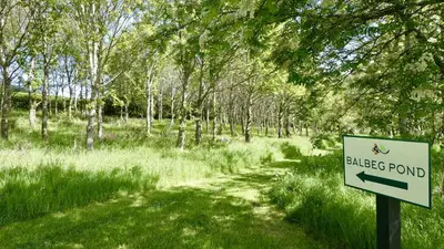 a sign for a black pond in a field with trees at Rabbie Burns Lodge in Maybole