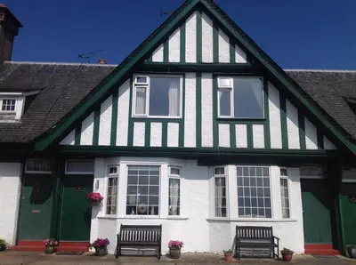 a white and green house with two benches in front at Eilean View in Lamlash