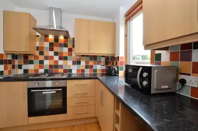 a kitchen with wooden cabinets and a microwave and a stove at Freeland Cottage in Dunoon