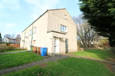 a white house with two trash cans in a yard at Penilee Upper Apartment in Glasgow
