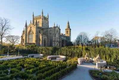 two people sitting on benches in a garden in front of a building at The Inn At Charlestown in Dunfermline