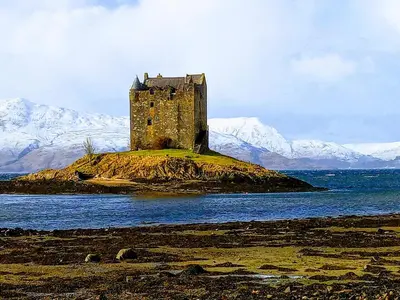 a castle on an island in the water with mountains at Granite Croft in Appin