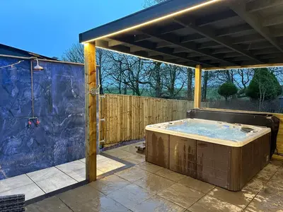 a hot tub in a patio with a wooden fence at The Hideaway - Farm Stay with hottub, pool table and outdoor cinema in Newmilns