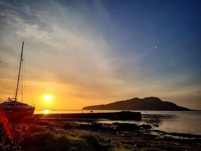 a boat sitting on the beach at sunset at Cosy cottage with sea views close to local shops. in Lamlash