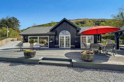 a house with a patio with a red umbrella at Little Fox Lodge Luxury Hideaway with Hot Tub Glencoe Near Fortwilliam in Glencoe