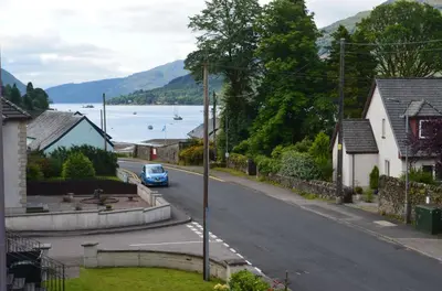 a blue car driving down a street next to a lake at Ben Arthur Place 6 - Sleep 6 in Lochgoilhead