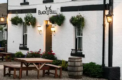 a white building with a picnic table in front of it at Black Bull Gartmore in Stirling