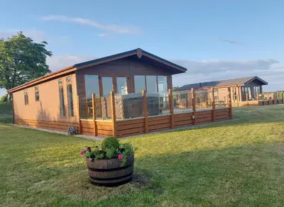 a large wooden house in a field with a yard at 2 Bedroom Sleeps 4 Lodge-Smart Tv-Hot tub-Dogs Ok in Lochwinnoch
