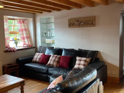 a living room with a black leather couch with red pillows at Mawenyoupe in Lochgilphead
