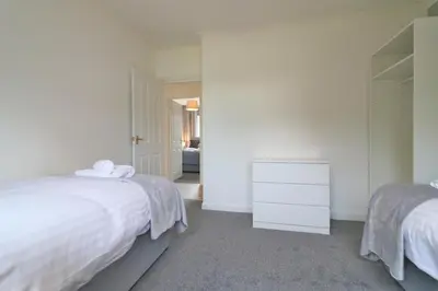 a white bedroom with two beds and a dresser at Macintosh lower in Bellshill